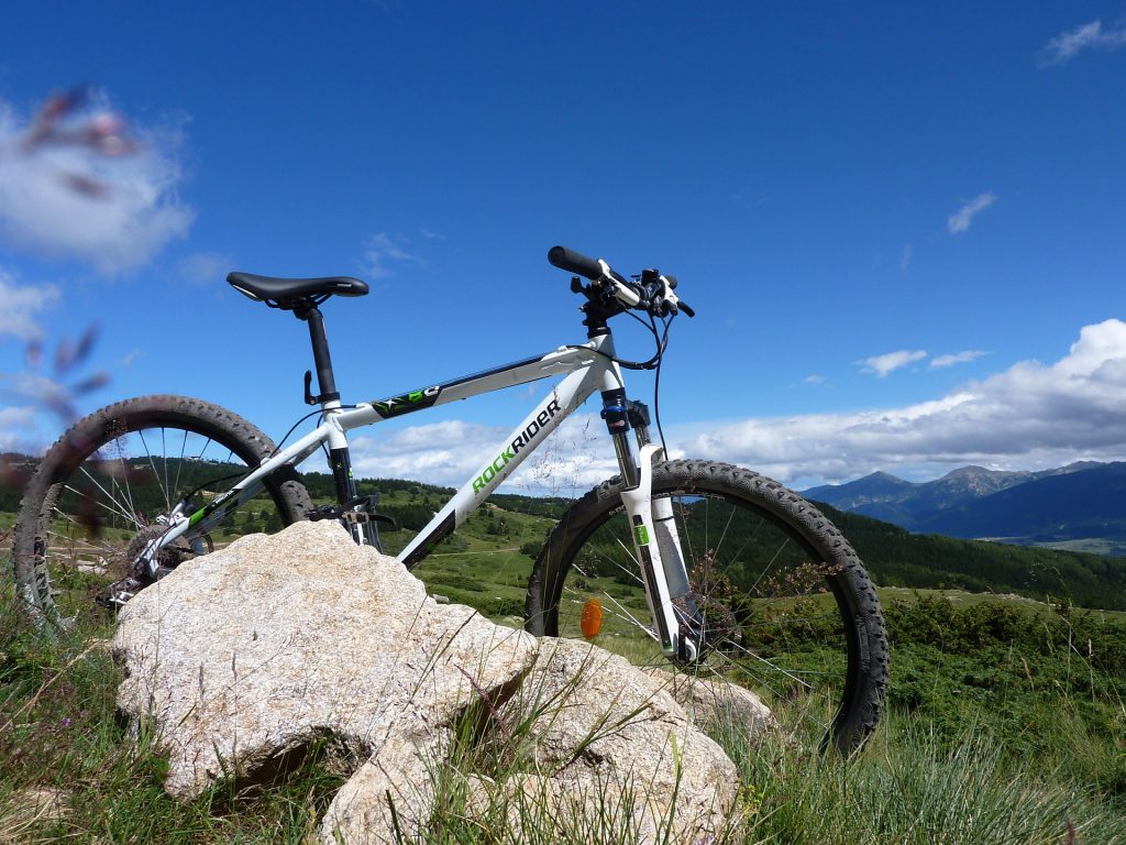 Un vtt posé debout derrière un gros caillou avec la montagne en fond