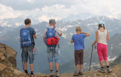Quatre personnes d'une famille vues de dos en tenues de randonneurs face à une montagne